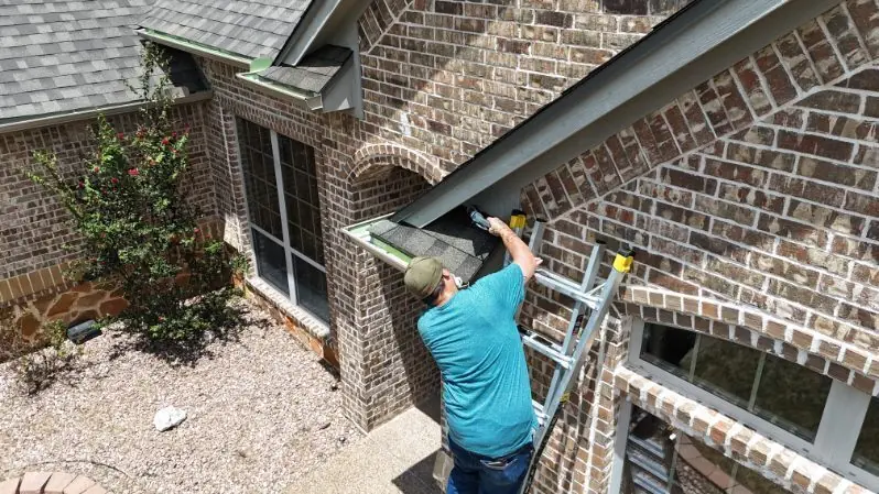An ACS fitter on a ladder working on the gutter line of a brick house