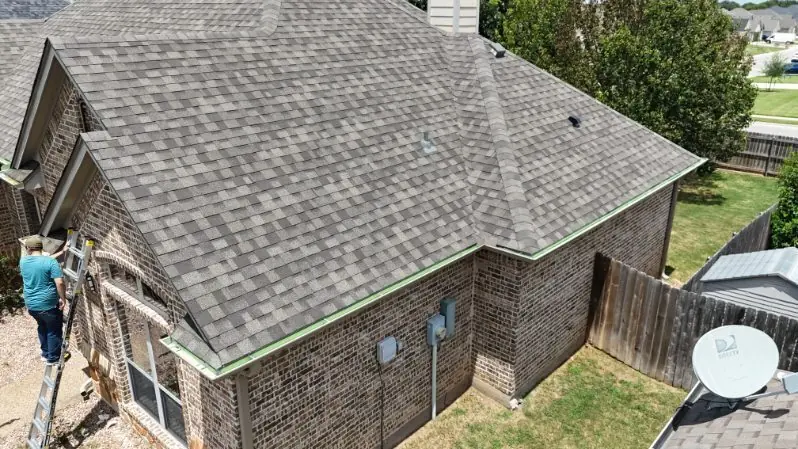An ACS fitter on a ladder working on the gutter line of a brick house
