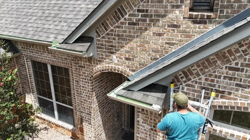 An ACS fitter on a ladder working on the gutter line of a brick house